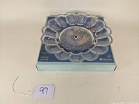 Clear glass vintage deviled egg server placed on original Indiana Glass box with blue and white design, showing front and top views.