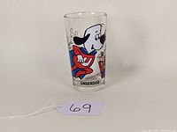 Glass side view showing Underdog cartoon character in mid-flight with red cape and city buildings in background.