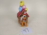 Front view of vintage Schmid Disney Pluto music box in front of doghouse with birthday balloons.