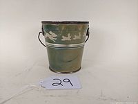 Front view of green metal peanut butter bucket with white running bunnies and puppies design, showing handle and lid edge.