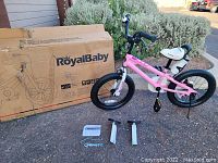 Photo of new RoyalBaby girls pink bicycle sitting outside near box and assembly tools.