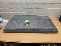 Top view of the rectangular gray memory foam dog bed with a soft cover and green plush toy on top.