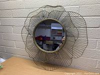 Front view of decorative wall mirror showing round mirror center and gold wire frame shaped like petals.