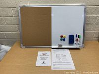 Front view of a combination dry erase whiteboard and corkboard on a table with accessories and paperwork in front.