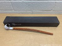 Gstar long stem pipe placed on black Gstar branded box against a brick wall background.