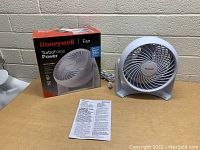 White Honeywell TurboForce Power fan, original box, and instruction manual on a wooden table with power cord visible
