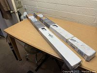 Two long rectangular boxes containing the blinds on top of a table and chair.