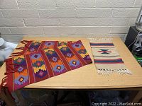 Both tapestries laid flat on a table showing overall pattern and size difference.