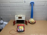 Three vintage Fisher-Price toys displayed on table with barn, push toy, and pull phone
