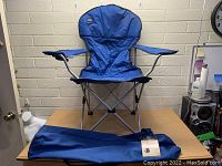Blue Mac Sports Belle camping chair set up with matching blue carry bag on a table in a room.