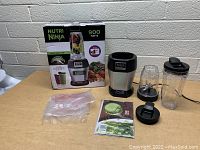 Nutri Ninja blender set with all components laid out on table including base, blending cup, blades, lids, and original box.