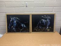 Both framed velvet paintings displayed on a table against a brick wall, showing matador and bullfighting scenes.