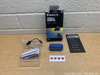 Skullcandy Totally Wireless Essential earbuds in blue with charging case, USB charging cable, four red earbud tip covers, user manual and original box arranged on a table against light gray wall.