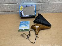 Photo of ceramic ocarina flute, instruction booklet, carrying case, and packaging box on table against brick wall background.