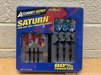 Front packaging photo showing three assembled Accudart Saturn soft tip darts with blue holographic flights, case, extra red flights and shafts visible.