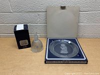 Photo showing the crystal bell in its black box and the crystal plate in its box with foam insert and lid behind.