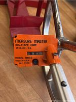 Close-up of the orange mechanical counter labeled MEASURE MASTER, Rolatape Corp., Model MM30, showing distance reading and mounting on metal frame.