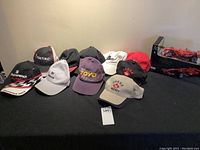 Shows 10 assorted ball caps with visible brand logos and the remote control car in package in the background.