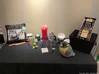 Full overview of all items on black cloth surface including BBQ tools, pillow, bird feeder, mugs, cups, cookie cutters and other small kitchen items.