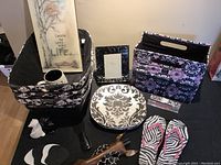 Photo showing black and white home decor and kitchen items including wall plaque, storage baskets, plates, mug, coasters, figurine, and flip flops.