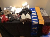 Photo showing assortment of hats, mittens, scarves, and slippers laid out on a black surface.