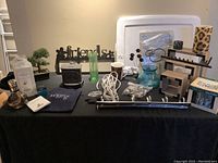 Wide shot of assorted home decor items on black cloth, showing faux bonsai tree, frames, hooks, green glass vase, and other items.