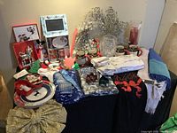 Full view of Christmas decor items including mugs, wreath, scarves, T-shirts, plates, large glittery bow and a crystal vase.