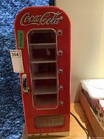Front view showing Coca-Cola logo, clear door with shelves, and dispensing lever, with lot sticker.