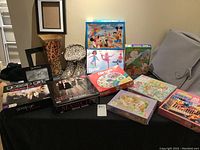 Overall view of the lot showing all puzzles, games, picture frames, vase, boots, and coin purse arranged on or near furniture