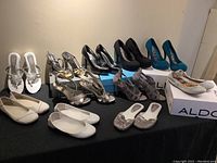 Full overview of 12 pairs of ladies shoes including flats, heels, and sandals arranged on a black cloth with two ALDO shoe boxes visible.