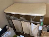 Front view of laundry sorter with ironing board top and three fabric bins below.
