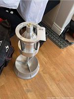 Full view of the aluminum manual wheel balancer showing base, springs, and central spindle.