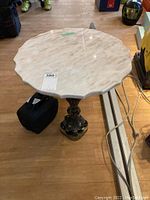 Photo of entire round marble top table with scalloped edges and ornate metal pedestal base on wood floor.