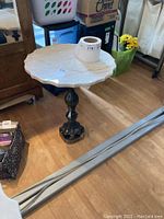 Full view of marble topped table with scalloped edge and ornate metal base on wooden floor.