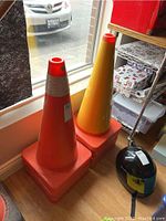 Stack of orange traffic cones and one yellow cone against window and shelf.