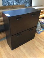 Front view of black 2-door shoe cabinet with drop front doors and black handles.