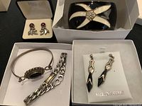 Close-up of smaller sterling silver earrings with round purple stones and leaf motif and other pieces arranged behind.