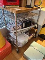 Full side view of 3-shelf metal trolley cart with wooden top and contents on shelves, some fabric liners, and items not included in sale.