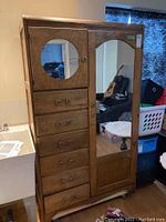 Front view of vintage wooden armoire showing full-length mirrored right door and smaller left door with circular mirror above six drawers.