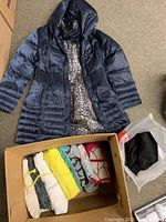 Navy blue winter coat laid flat showing leopard print lining and ribbed sides, box of folded hoodies and sweaters