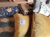 Photo of assorted decorative pillows in various colors and sizes, including mustard yellow velour pillows, floral and tapestry-style pillows with tassels and fringe.