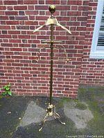 Full view of the brass valet stand showing overall height, hanger, adjustable arms, and tripod base.