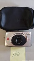 Front view of Leica Z2X camera with lens, flash, and Leica logo, alongside black carrying case.