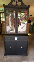 Front view of the refurbished black china cabinet showing glass pane double doors with wood lattice, drawer, and lower cabinet doors.