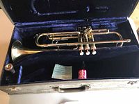 Conn 77B trumpet shown inside open case, also showing valve oil bottle and certificate or documentation inside case.