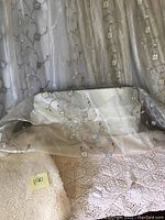 Photo of three cream sheer curtain panels with embroidered floral design draped over a crochet bedspread and a piece of sherpa fabric