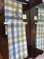 Two plaid curtain panels with blue, cream and green colors hanging on a rod in front of a mirror.