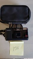 Photo showing the Konica A4 camera with lens, flash, and front details alongside a black zippered camera case.