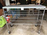 Front view of metal shelving unit on wheels showing two wire shelves and metal top.
