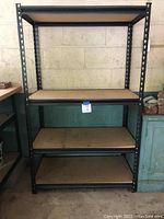 Full view of the metal utility shelving unit showing four particle board shelves and black metal frame.